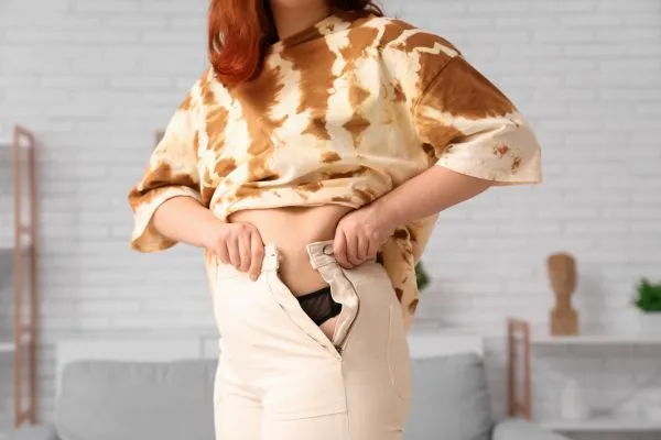 Image of woman trying to do her trousers up after pregnancy weight gain Stamford